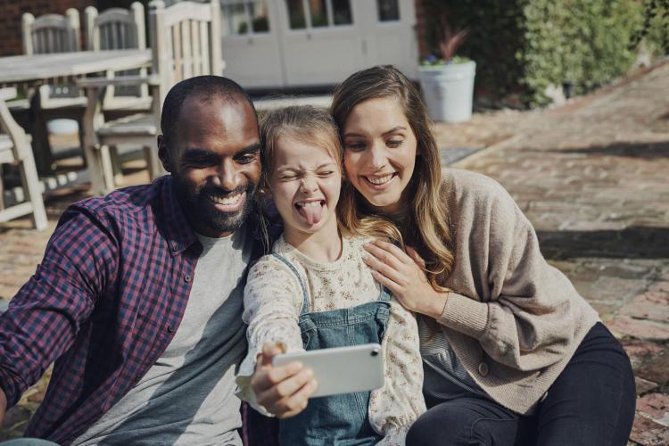 Joven levantando su m&oacute;vil para hacer una foto con sus padres.